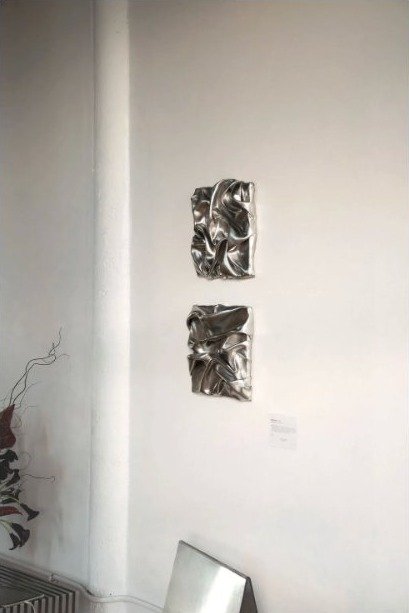 Deux œuvres murales argentées plissées accrochées sur un mur blanc
