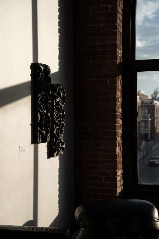 Œuvre murale noire texturée près d’une fenêtre, mur de briques