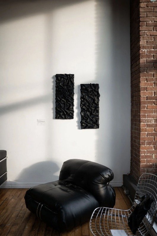 Deux œuvres murales noires texturées au-dessus d’un fauteuil en cuir